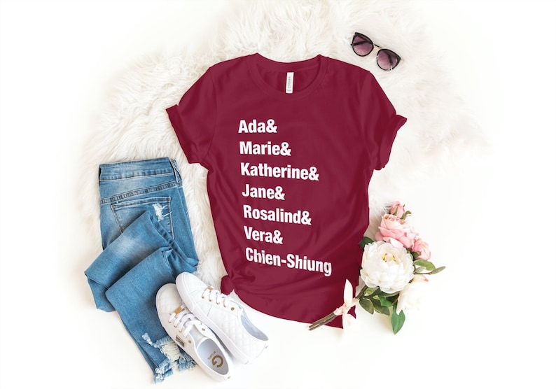 May include: A maroon t-shirt with white text that reads "Ada & Marie & Katherine & Jane & Rosalind & Vera & Chien-Shiung".