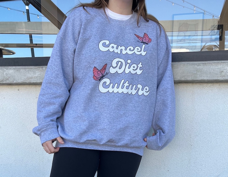 Pu&ograve; includere: Felpa grigia con il testo "Cancel Diet Culture" in bianco con grafiche di farfalle rosa.
