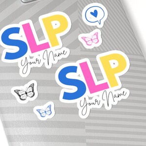 May include: Two white stickers with the letters "SLP" in blue, pink, and yellow. The stickers have the text "Your Name" written in black cursive. There are also four smaller stickers with butterfly and heart designs.