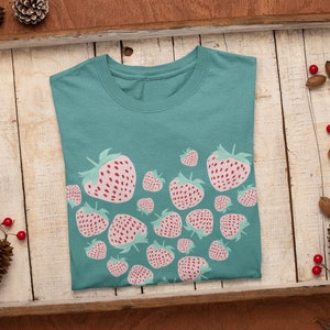 May include: A teal blue t-shirt with a heart-shaped design made up of pink and red strawberries.