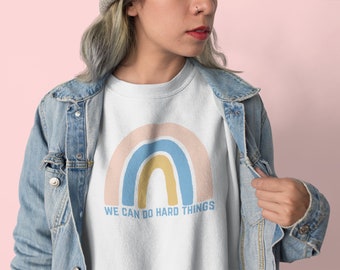 May include: White sweatshirt with a rainbow graphic and the text "WE CAN DO HARD THINGS".