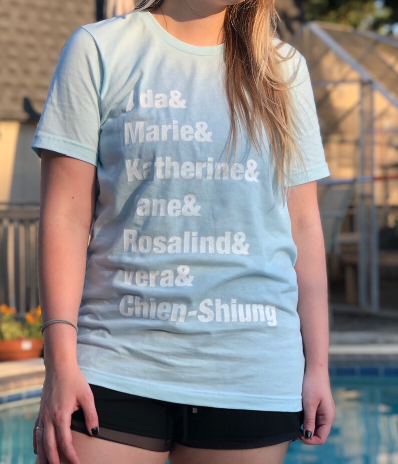 May include: A light blue t-shirt with white text that reads "da& Marie& Katherine& ane& Rosalind& vera& Chien-Shiung".
