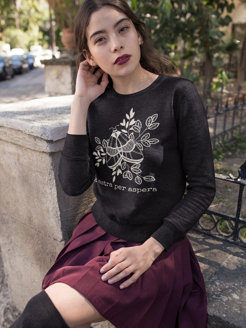 Op de afbeelding: Een zwart longsleeve sweatshirt met een wit mot- en bladmotief. De tekst "ad astra per aspera" is onder het ontwerp gedrukt.