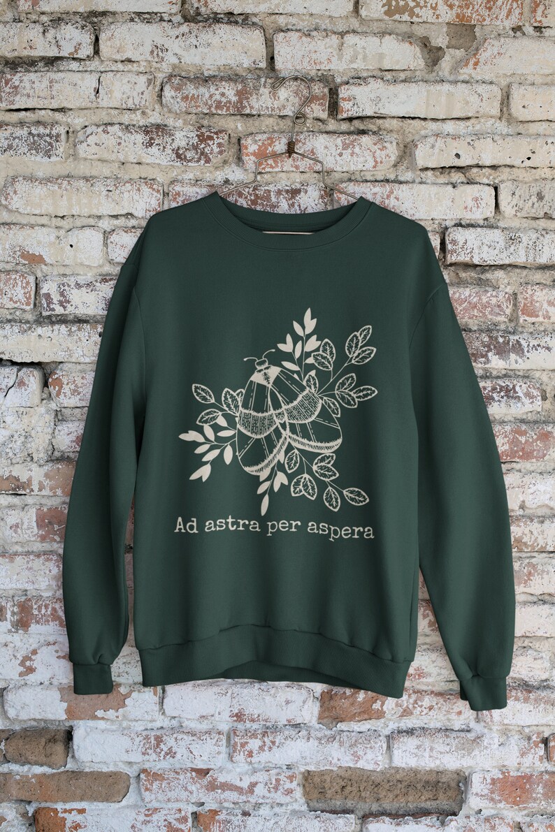 Op de afbeelding: Een donkergroen sweatshirt met een witte afbeelding van twee motten op een tak met bladeren. De tekst "Ad astra per aspera" is onder de afbeelding gedrukt.