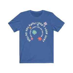 May include: A royal blue t-shirt with a white circle design featuring the text "How do you know I don't look like my doctor sick?" with colorful flower graphics around the text.