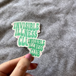 May include: Two green and white stickers with the text "Invisible Illness Club" in a retro font. The stickers have pink hearts around the text.