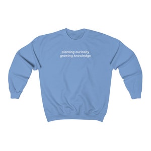 Puede incluir: Una sudadera azul claro con el texto "planting curiosity growing knowledge" impreso en blanco en la parte delantera.