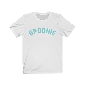 May include: White t-shirt with the word "SPOONIE" printed in a light blue color in an arched font.
