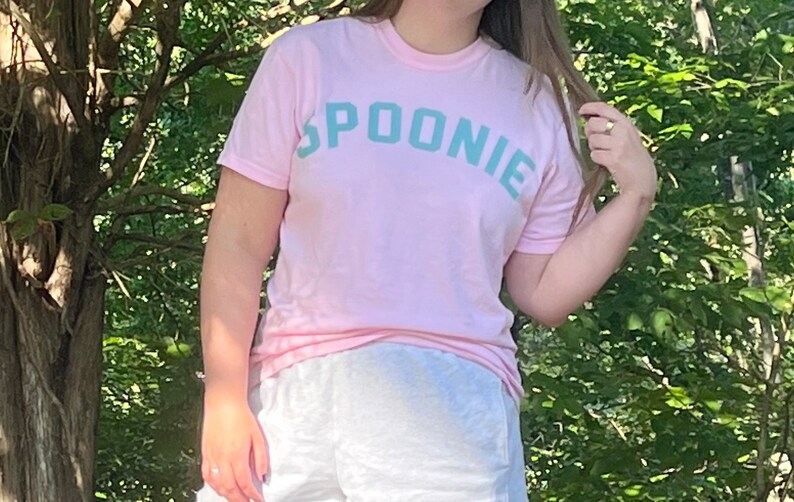 May include: A pink t-shirt with the word "SPOONIE" printed in teal blue letters.