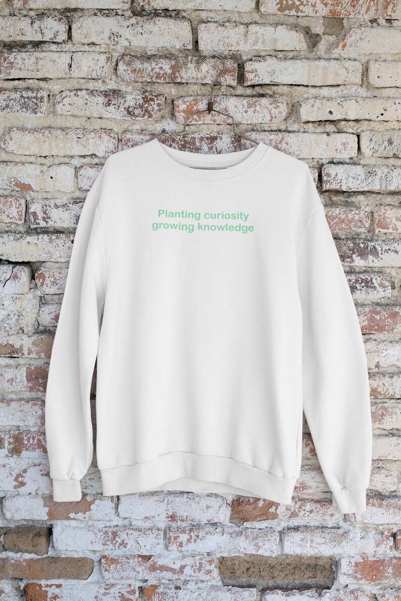Puede incluir: Sudadera blanca con un gr&aacute;fico de texto verde que dice "Planting curiosity growing knowledge".