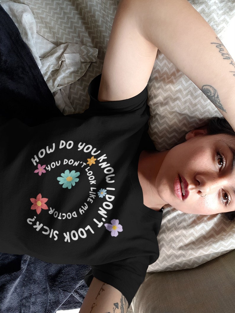 May include: Black t-shirt with a white graphic design that says "How do you know I don't look sick?" with a floral design around the text.