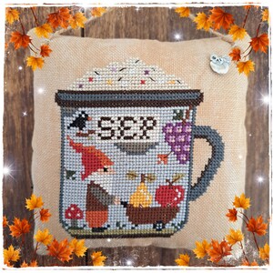Può includere: Un cuscino beige con un ricamo a punto croce di una tazza con un gnomo e la parola "Soup" su di essa. La tazza è piena di una sostanza bianca e ha un manico. Il gnomo indossa un cappello rosso e tiene una pera. Ci sono uva e funghi intorno alla tazza.