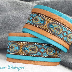 Puede incluir: Dos pulseras de cuero en turquesa y marrón. Las pulseras presentan un patrón detallado en tonos marrones, dorados y azules. Las pulseras están apiladas, con el texto "Luca-Design" en la esquina inferior izquierda. Un accesorio elegante.
