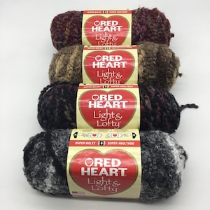 以下が含まれることがあります： 異なる色の組み合わせで、Red Heart Light & Lofty 糸の4玉。糸はスーパーバルキーで、ふわふわした質感です。ラベルは赤で、白いハートと白い文字で「Red Heart Light & Lofty」と書かれています。