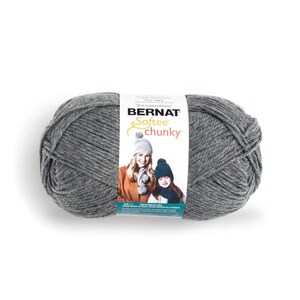 Könnte beinhalten: Ein Knäuel graues, dickes Garn mit einem weißen Papieretikett, das den Text Bernat Softee chunky, Yarnspirations sowie ein Foto von zwei Personen mit Strickmützen zeigt. Das Etikett gibt ein Gewicht von 400 g für dieses Bastelmaterial an.