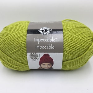 May include: A skein of Loops & Threads Impeccable yarn in a bright green color. The label features the brand name and the yarn name, "Impeccable". A free pattern for a red beanie is included.