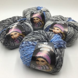 Può includere: Quattro gomitoli di lana in tonalità di grigio, nero e blu con un'etichetta bianca che dice "Magdalena Neuner" e raffigura una donna con un cappello e una sciarpa.