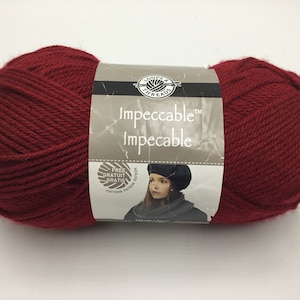 Puede incluir: Un ovillo de hilo Impeccable de Loops & Threads de color rojo oscuro. La etiqueta dice "Impeccable" y muestra a una niña con una boina roja y una bufanda a juego.