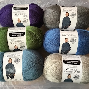 May include: Six balls of Woolike Simili-Laine yarn in shades of purple, grey, green, blue, and beige. Each ball has a label with the brand name and a woman's image. The yarn is 675 yds / 100 g. The yarn is 100 g.