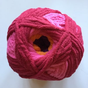 May include: A ball of yarn with a pink, orange, and purple color gradient. The yarn is soft and fluffy, and it is perfect for knitting or crocheting.