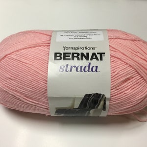 May include: A pink ball of Bernat Strada yarn, a 100% acrylic yarn. The label reads "Yarnspirations™ BERNAT strada." and "NET WEIGHT POIDS NET PESO NETO 10 oz (283 g) 617 yds/vgs/yds/564m".