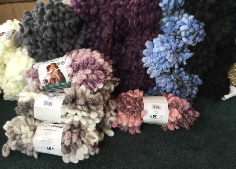 Puede incluir: Surtido de hilo Bernat Blanket en varios colores, incluyendo blanco, gris, morado, rosa y azul. El hilo es de estilo esponjoso y texturizado.