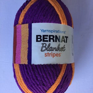 May include: A ball of Bernat Blanket Stripes yarn in purple and orange. The label reads "Yarninspirations Bernat Blanket Stripes".
