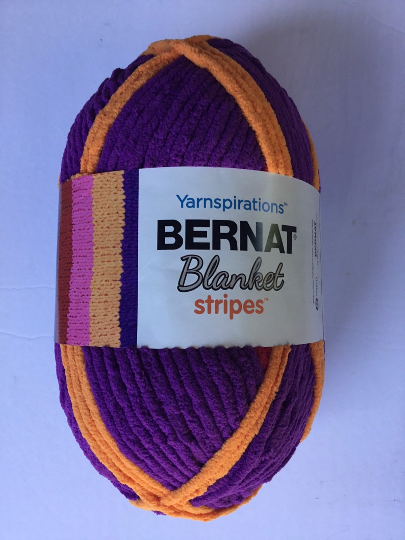 May include: A ball of Bernat Blanket Stripes yarn in purple and orange. The label reads "Yarninspirations Bernat Blanket Stripes".