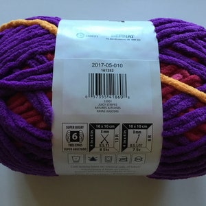 May include: A skein of Bernat Super Bulky yarn in the color Juicy Stripes. The yarn is a mix of purple, pink, and yellow. The label shows the yarn weight, needle size, and care instructions.