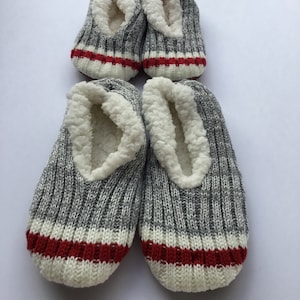 May include: Pair of grey knitted slipper socks with white and red stripes. The slippers have a white fleece lining.