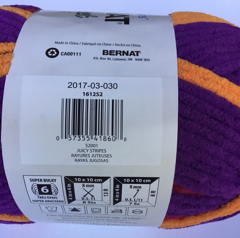 May include: A purple and orange yarn ball with the brand name "Bernat" and the product name "Juicy Stripes". The yarn is super bulky and has a 6 on the label. The label also includes the size and gauge information.