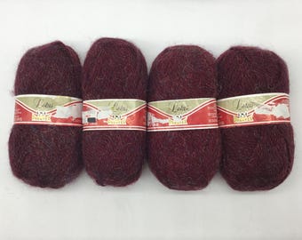 May include: Four skeins of burgundy yarn with a fuzzy texture. Each skein has a label that reads "Lotus Phentex".