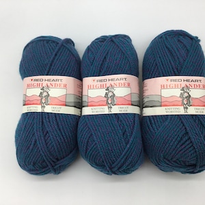 Peut inclure: Trois pelotes de laine bleu et violet étiquetées "Red Heart Highlander" tricot.