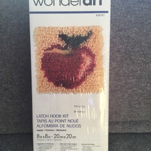 May include: A Wonderart latch hook kit featuring an apple design. The kit includes materials to create a finished rug measuring 8 inches by 8 inches. The packaging displays the brand name and product details.