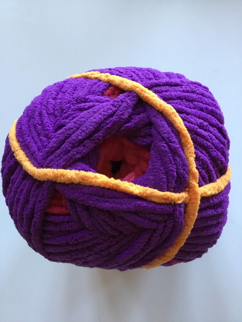 May include: A ball of purple yarn with a yellow stripe wrapped around it. The yarn is soft and fluffy, and it is perfect for knitting or crocheting.