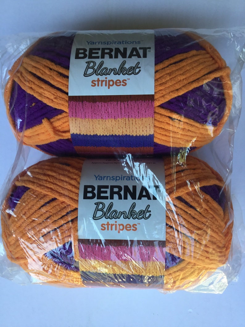 May include: Two skeins of Bernat Blanket Stripes yarn in orange, purple, pink, and yellow. The yarn is packaged in clear plastic.