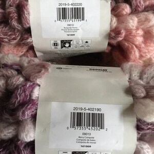 Puede incluir: Dos ovillos de hilo Bernat, uno en una combinaci&oacute;n de colores rosa y blanco llamada "Burgundy Peony" y otro en una combinaci&oacute;n de colores morado y blanco llamada "Berry Compote". Ambos ovillos tienen un aspecto peludo y texturizado.