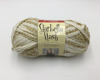 May include: A skein of Premier Yarns Starbella Flash yarn in a cream color with gold metallic thread. The label reads "Starbella Flash" and lists the yarn content as 86% acrylic and 14% metallic.