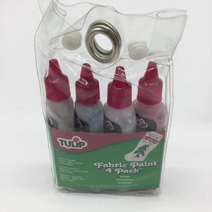 May include: A clear plastic bag with a silver grommet and four bottles of Tulip Fabric Paint in a 4-pack. The bottles contain glitter paint in the colors gold, ruby, green, and silver. The label reads "Fabric Paint 4 Pack" and "Glitter Brillantina Palettes".