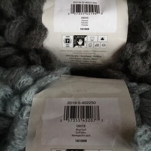 Puede incluir: Dos ovillos de hilo, uno negro y otro azul. El hilo tiene una textura esponjosa y voluminosa. Las etiquetas de los ovillos incluyen informaci&oacute;n del producto, como el peso del hilo, el contenido de la fibra y el nombre del color. Las etiquetas tambi&eacute;n incluyen c&oacute;digos de barras y el texto "161009".