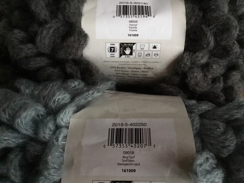 Puede incluir: Dos ovillos de hilo, uno negro y otro azul. El hilo tiene una textura esponjosa y voluminosa. Las etiquetas de los ovillos incluyen informaci&oacute;n del producto, como el peso del hilo, el contenido de la fibra y el nombre del color. Las etiquetas tambi&eacute;n incluyen c&oacute;digos de barras y el texto "161009".