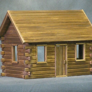 Finished 1-inch scale Crocketts Log Cabin Dollhouse Kit by Real Good Toys. Front view of rustic log cabin dollhouse made with log siding. Size 13.5 inches tall x 18 wide. Kit sold unfinished.