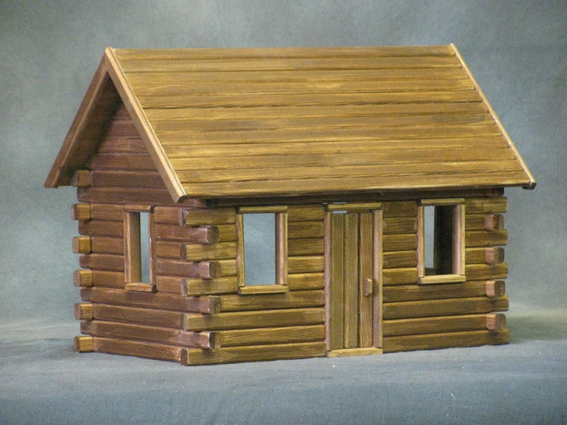 Finished 1-inch scale Crocketts Log Cabin Dollhouse Kit by Real Good Toys. Front view of rustic log cabin dollhouse made with log siding. Size 13.5 inches tall x 18 wide. Kit sold unfinished.