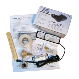 May include: A dollhouse wiring kit with a 40 watt tabletop transformer, a spool of white electrical tape, a small wooden dowel, a bag of small gold-colored metal eyelets, a bag of larger gold-colored metal eyelets, a small white plastic brush, a small white plastic block, a small black plastic block, a small black plastic switch, a small black plastic plug, a small black plastic cord, and a small black plastic box with the text "CIR-KIT" on it.