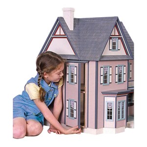 Young girl demonstrating unique side opening access to 1 inch scale Victorias Farmhouse Dollhouse Kit by Real Good Toys. 3 story farmhouse 33 in. tall x 34.5 wide. Milled clapboard exterior, wrap around porch, wood roof shingles. Kit is unfinished.