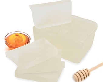 May include: A stack of clear, rectangular soap bars with a small bowl of honey and a honey dipper.