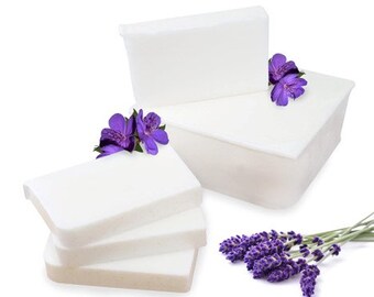 May include: Three white rectangular bars of soap with a stack of two on the left and a single bar on the right. The soap bars are decorated with purple flowers and lavender sprigs.