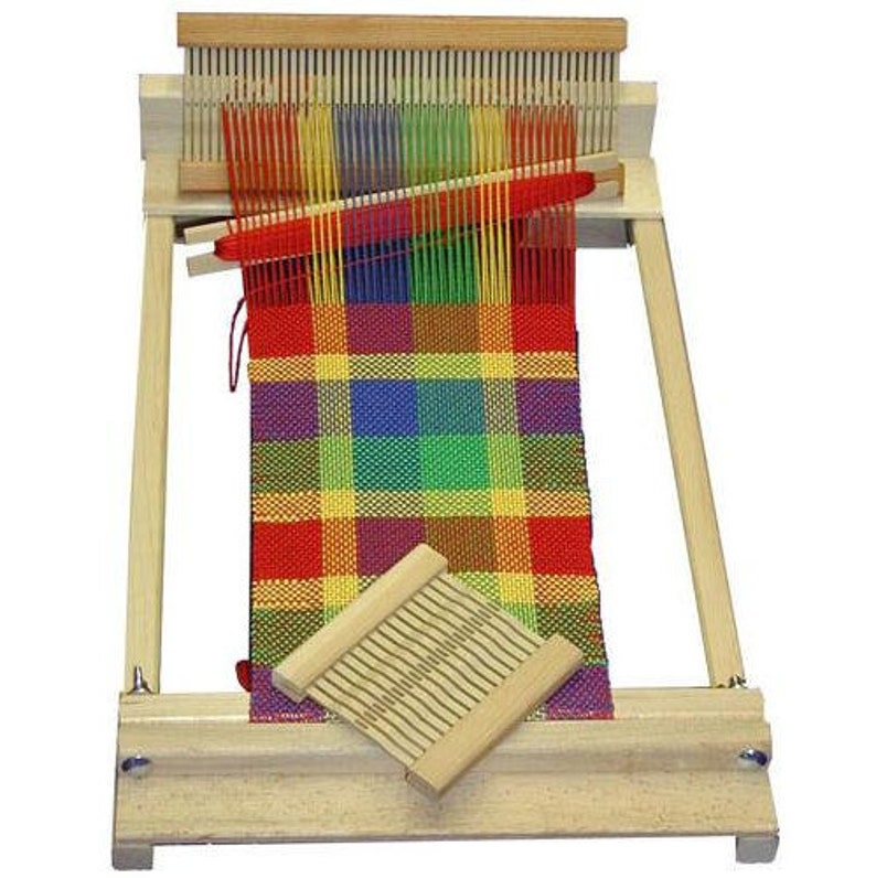 May include: A wooden loom with a colorful plaid fabric woven on it. The loom has a wooden frame and a shuttle for weaving.
