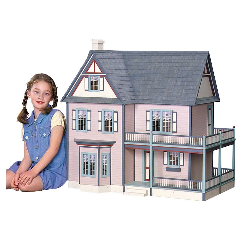 Young girl sitting next to finished 1 inch scale Victorias Farmhouse Dollhouse Kit by Real Good Toys. 3 story farmhouse 33 in. tall x 34.5 wide with milled clapboard exterior, wrap around porch, and wooden roof shingles. Kit is unfinished.