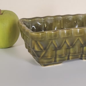 May include: An olive green ceramic planter with a basket weave pattern. The rectangular planter is empty and next to a green apple. The planter is approximately 20 cm long.
